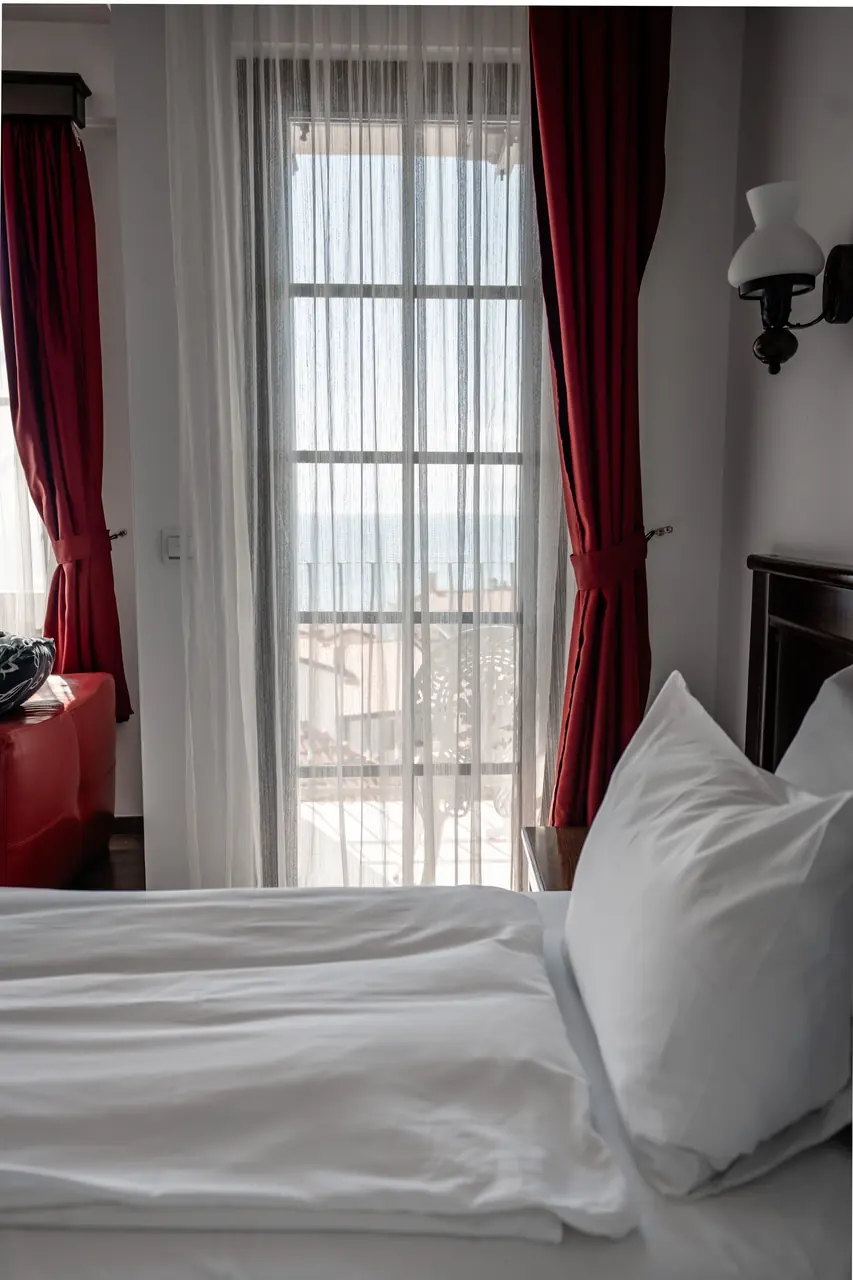 Corner of the bed by a tall window with sheer curtain, portrait