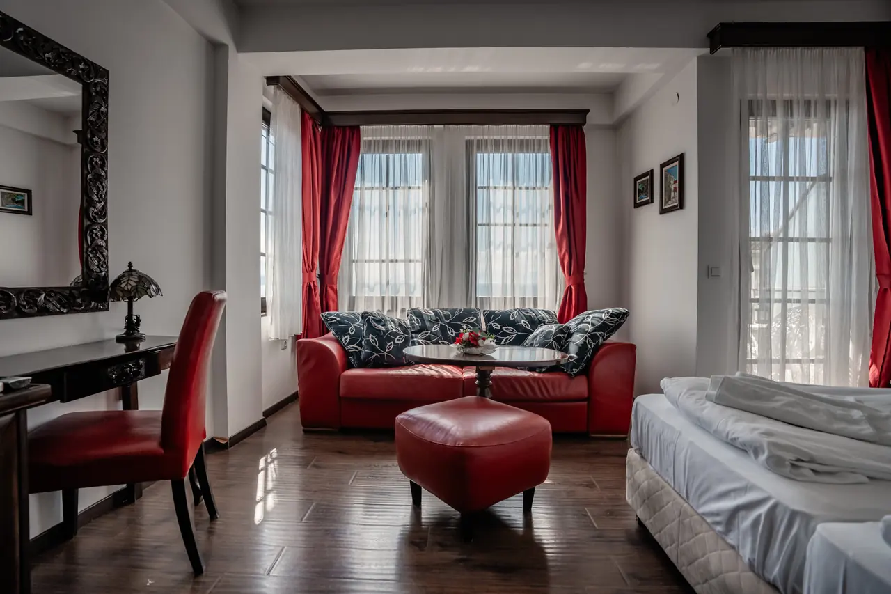 Seating area: red leather sofa, ottoman, red curtains, bright windows