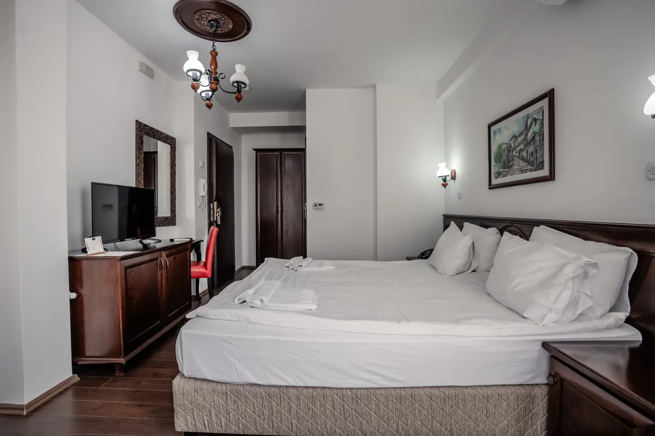 Bed toward the door, chandelier and TV