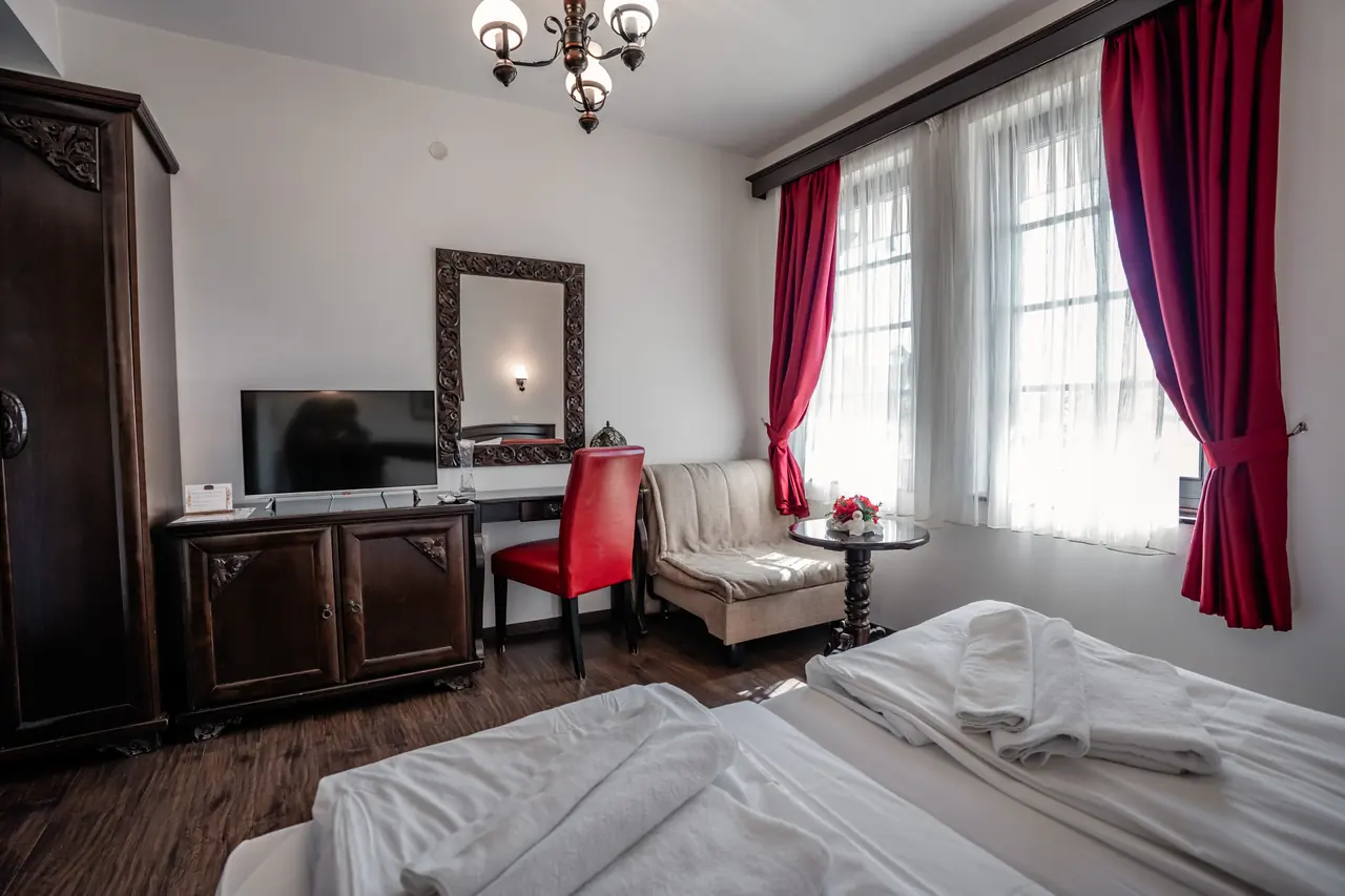 Bed, desk with red chair, sofa by windows with red curtains