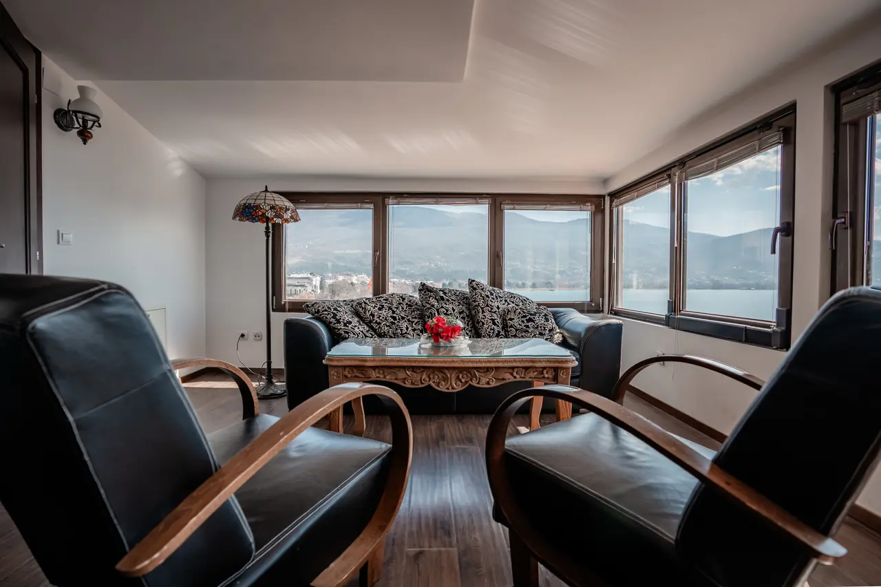 Living room: two leather armchairs in front, sofa and wraparound windows onto the lake