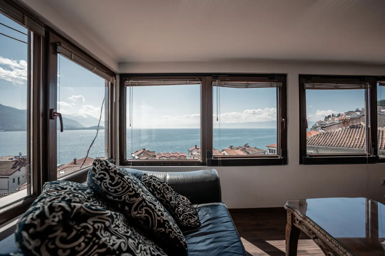 Sofa with patterned cushions against the corner windows, lake and old-town roofs outside