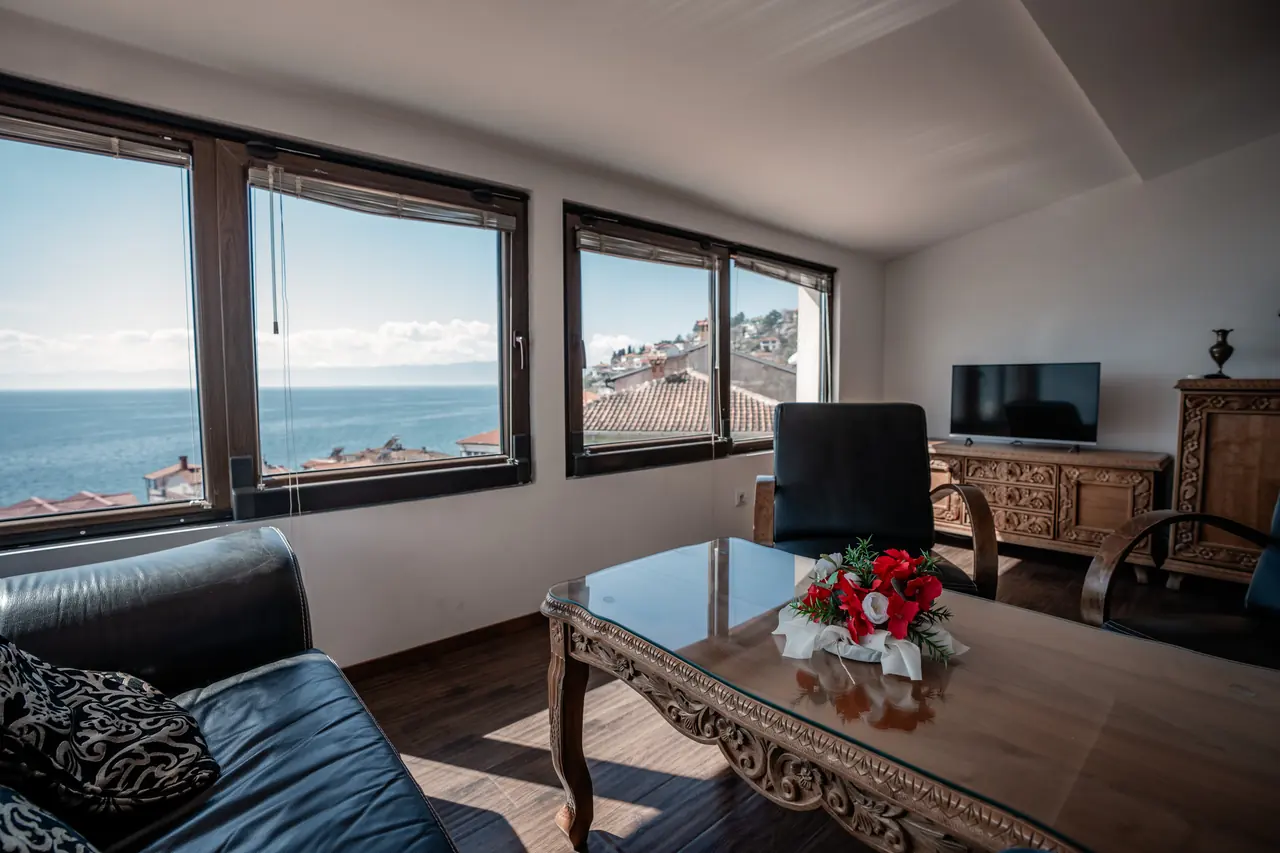 Carved coffee table with flowers, sofa, lake through the windows, TV on the right