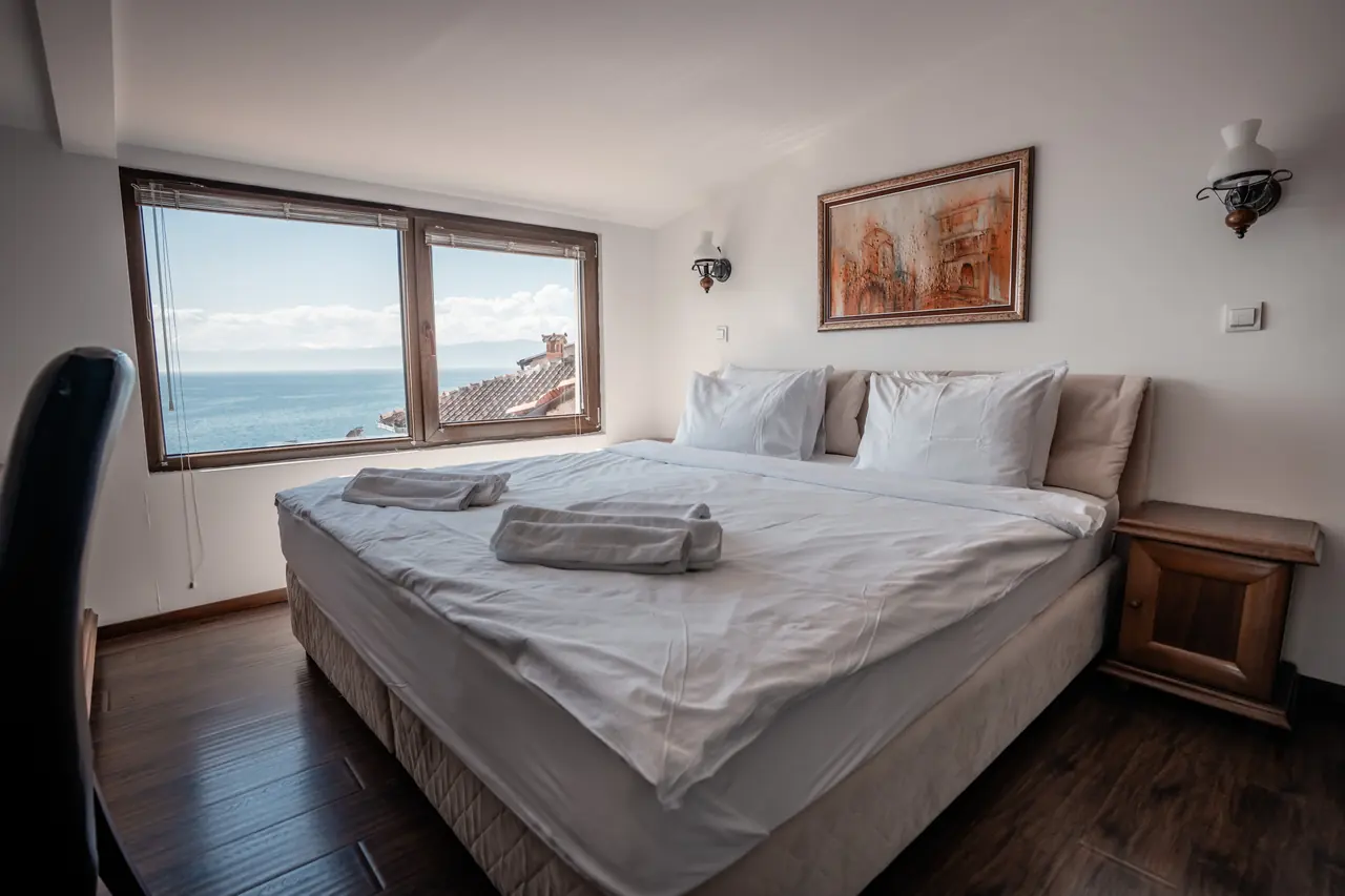 Bedroom: double bed facing a window onto the lake, painting above