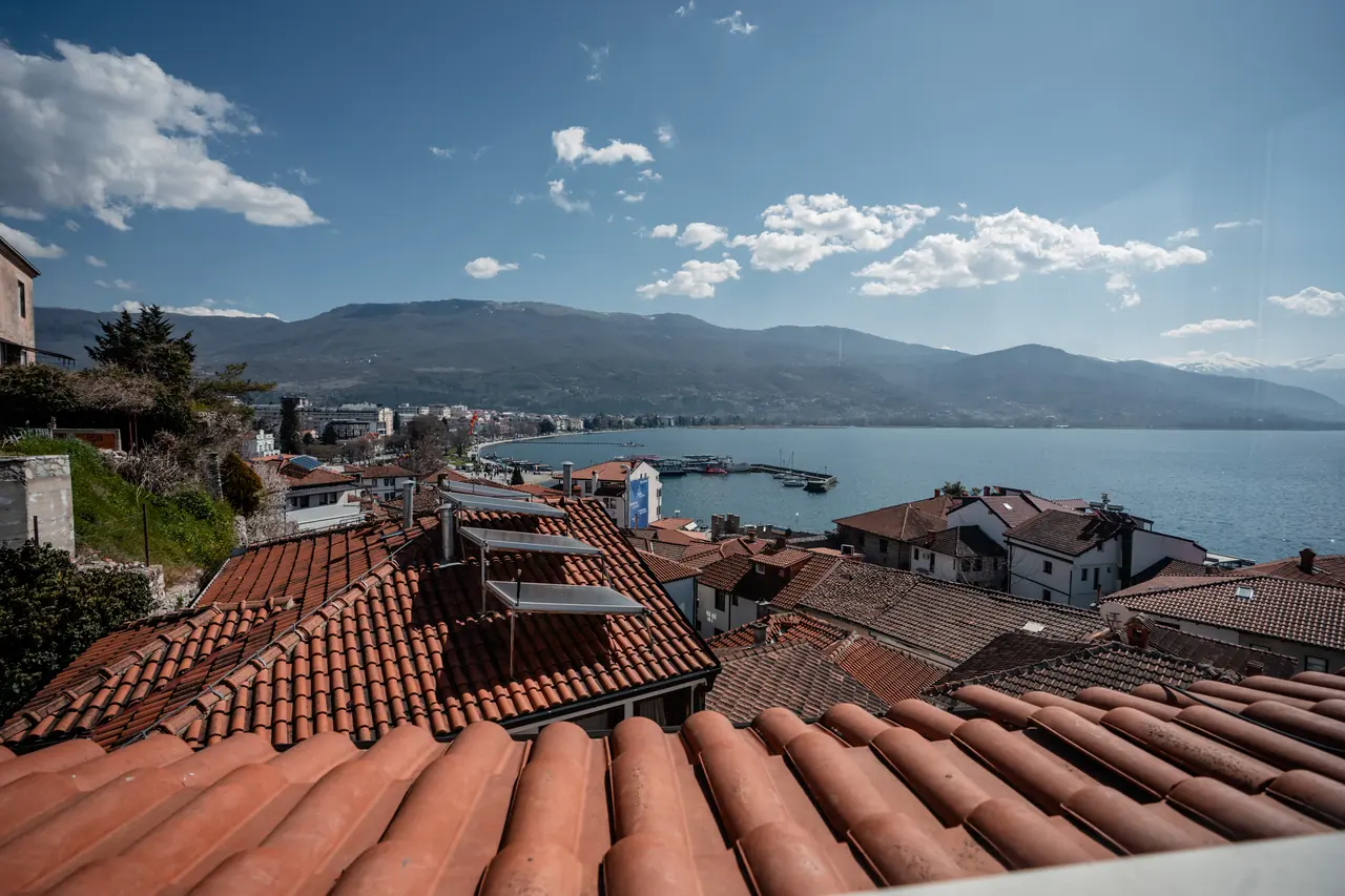 View from the penthouse: red-tile roofs, harbour, lake and mountains under blue sky