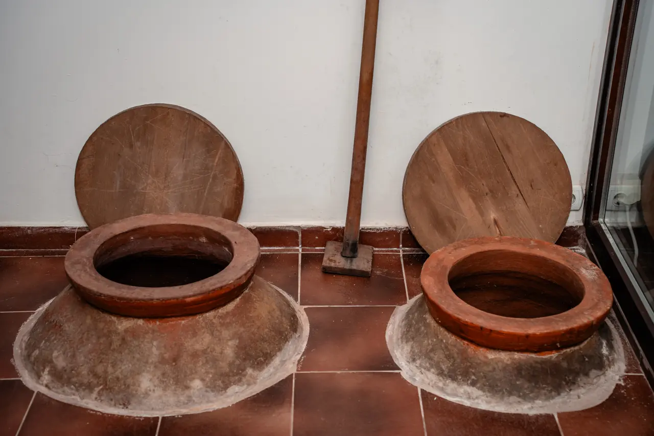 Two clay amphorae set into the cellar floor with their wooden lids open